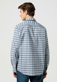 Camicia a maniche lunghe a quadretti in azzurro chiaro e navy, con colletto classico e polsini con bottone, dotata di un orlo leggermente curvo.