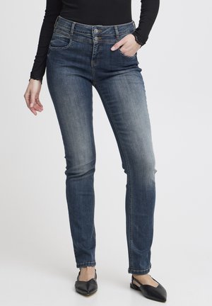 Eng anliegende dunkelblaue Jeans mit leichtem Verblassen, mittelhohem Bund, doppeltem Knopfverschluss und vorderen Taschen. Kombiniert mit schwarzen Ballerinas.