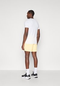 Λευκό κοντομάνικο πουκάμισο, κίτρινες σορτς, μαύρα αθλητικά παπούτσια με λευκές λεπτομέρειες, λευκές κάλτσες μέχρι τον αστράγαλο. Απαλή υφή, άνετος αθλητικός σχεδιασμός.