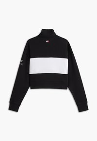 Bluza alb-negru decupată, cu mâneci lungi, guler înalt și logo mic pe partea superioară a pieptului și pe mâneca stângă.