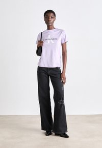 T-shirt de algodão lilás claro com o logótipo da Calvin Klein, combinado com jeans flared pretos de cintura alta com detalhes desgastados.