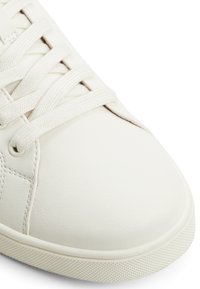 Białe sneakersy skórzane o teksturowanej powierzchni, okrągłym nosku i subtelnych detalach haftu. Posiadają płaskie sznurowanie i teksturowaną gumową podeszwę.
