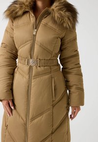 Cappotto puffer khaki con cappuccio foderato in pelliccia, dotato di una vita con cintura, chiusura con zip e motivi a rombi diagonali. Texture liscia, maniche lunghe.