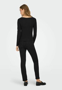 Zwarte langemouwen top in combinatie met zwarte skinny jeans en zwarte loafers, met een aansluitend ontwerp en een gladde textuur.