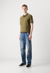Oliven grøn polo skjorte med korte ærmer, blå falmede jeans og sorte sneakers. Simpelt design med krave og en diskret logo.