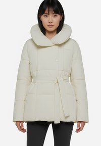 Giubbotto imbottito di colore crema con un ampio colletto arrotondato, vita cintata e maniche lunghe e larghe. Presenta una superficie liscia e trapuntata.