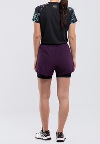 Svart atletisk tröja med blommönstrade ärmar, i kombination med lila shorts över svarta kompressionsshorts. Atletiska skor fulländar looken.