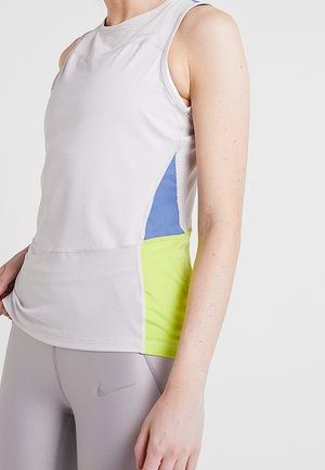 Haut de sport blanc sans manches avec panneaux latéraux bleus et jaune néon porté par une personne en leggings gris clair avec un logo Nike.