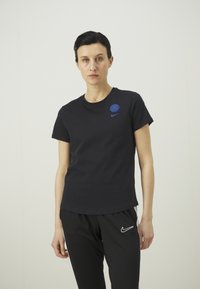 Čierne bavlnené tričko s okrúhlym výstrihom, s modrým logom na ľavej hrudi a priliehavým strihom. V súprave s čiernymi športovými nohavicami.