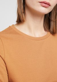 Bruine katoenen top met een ronde halslijn en korte mouwen, met een zachte textuur en subtiele naaddetails bij de kraag.
