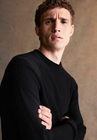 Schwarzer Strickpullover mit geripptem Rundhalsausschnitt und langen Ärmeln, der eine weiche Textur und eine körpernahe Passform bietet.