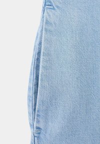 Tissu en denim bleu clair montrant une couture latérale et le bord de la poche avec double surpiqûre sur un fond uni.
