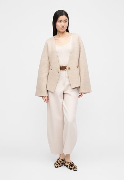 Μπεζ φαρδιά ζακέτα με δύο κουμπιά, φορεμένη πάνω από ανοιχτόχρωμη μπλούζα, συνδυασμένη με μπεζ παντελόνια φαρδιάς γραμμής και μοκασίνια με λεοπάρ μοτίβο.