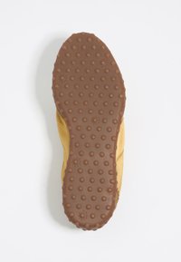 Scarpa gialla con suola in gomma marrone testurizzata caratterizzata da modelli di grip circolari. Materiale superiore morbido con dettagli di cucitura visibili.