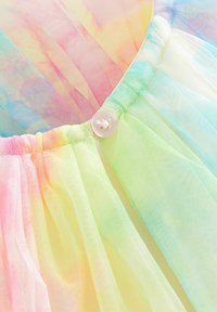 Gros plan d’un tissu en tulle arc-en-ciel pastel avec un bouton blanc cousu sur un matériau transparent froncé.