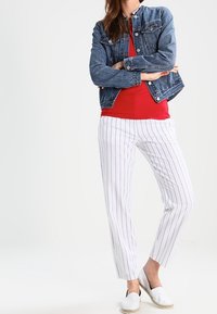 Jeansjacke, rotop, weiße gestreifte Hose und weiße Espadrilles. Die Jacke hat Blautöne; die Hose hat vertikale Streifen für einen lässigen Look.