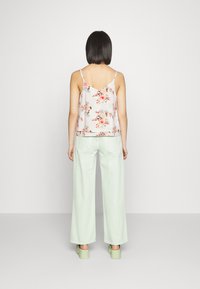 Top sem mangas floral em tecido leve, com flores rosa e azuis, emparelhado com calças largas verde menta e sapatos plataforma verdes.