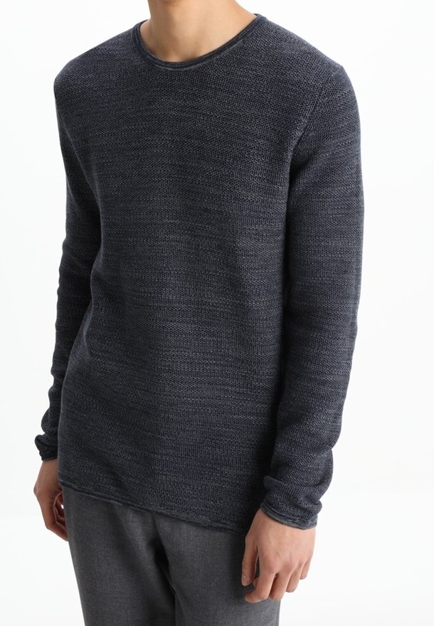 Dunkelblauer Rundhals-Pullover aus strukturiertem Stoff, mit langen Ärmeln und gerippten Bündchen. Kombiniert mit grauen Hosen. Schlichtes, modernes Design.