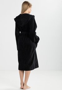Black hooded bathrobe made of soft, plush material, featuring a belt and side pockets, with a knee-length design and textured fabric.