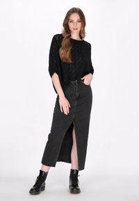 Top nero lavorato a maglia con vestibilità morbida e maniche corte, abbinato a una gonna maxi in denim nera con spacco frontale e lunghezza fino alla caviglia. Stivali neri.