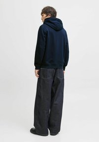 Námořnická mikina s kapucí v kombinaci s volnými tmavými džíny. Viditelné švy na kapsách. Hladká textilie. Jednoduchý design.