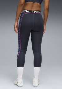 Collant di un blu navy scuro con strisce laterali rosa e una vita elastica nera con il testo "PUMA". Texture liscia, design aderente.