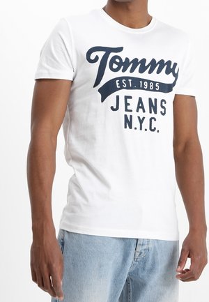 Biały bawełniany T-shirt z krótkimi rękawami, z ciemnoniebieskim nadrukiem logo z napisem "Tommy EST. 1985 JEANS N.Y.C." na środku.