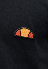 Μαύρο ύφασμα με μικρό κεντητό μισοκυκλικό σχέδιο που περιλαμβάνει μία μεγάλη πορτοκαλί ενότητα ανάμεσα σε δύο μικρότερες κόκκινες ενότητες με μαύρο περίγραμμα.