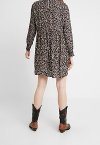 Vestido negro con flores, de mangas largas, cintura fruncida, tejido texturizado y falda de volantes. Combinado con botas vaqueras negras con acentos marrones.