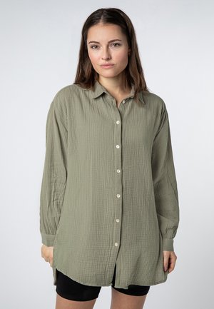 Olive green button-up shirt made of textured fabric, featuring a collared neckline, long sleeves, and a relaxed fit with side slits.
