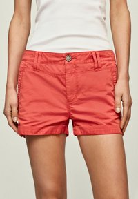 Pantalones cortos de algodón rosa con cierre de botón, trabillas para cinturón, dobladillo enrollado y bolsillos frontales. Textura suave y diseño informal adecuado para climas cálidos.