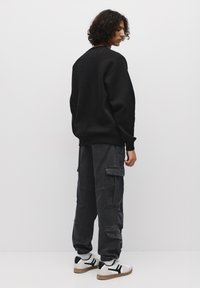 Hanorac negru cu o croială lejeră, asociat cu pantaloni cargo gri închis, care au multiple buzunare și manșete elastice. Adidași albi cu accente.