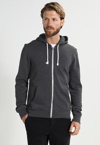Mørkegrå hettejakke med glidelås laget av mykt materiale, med snorhette, frontlommer og hvit glidelås. Enkel, uformell design.