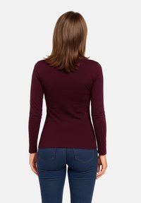 Top a maniche lunghe color bordeaux in tessuto elasticizzato, design aderente, con una texture liscia e scollatura rotonda, abbinato a jeans blu scuro.