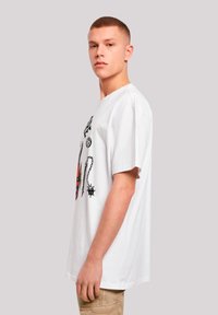 White cotton t-shirt with short sleeves, featuring graphic designs in black and red, relaxed fit, side view of a model.