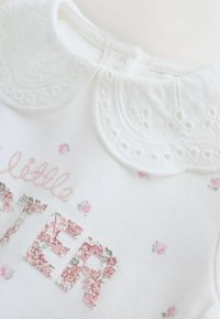 Fehér pamut body díszes csipkegallérral, virágmintákkal és a "SISTER" felirattal texturált rózsaszín anyagból.