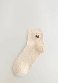 Ljusbeige bomullsstrumpor med ribbat mönster och en liten brun hjärtformad design broderad nära skaftet. Ankellång stil.