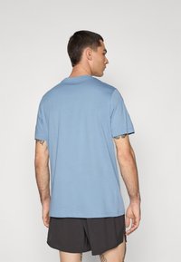 Světle modré bavlněné tričko s krátkými rukávy, kulatým výstřihem a volným střihem, nošené s černými šortkami. Jednoduchý design, bez vzorů nebo akcentů.