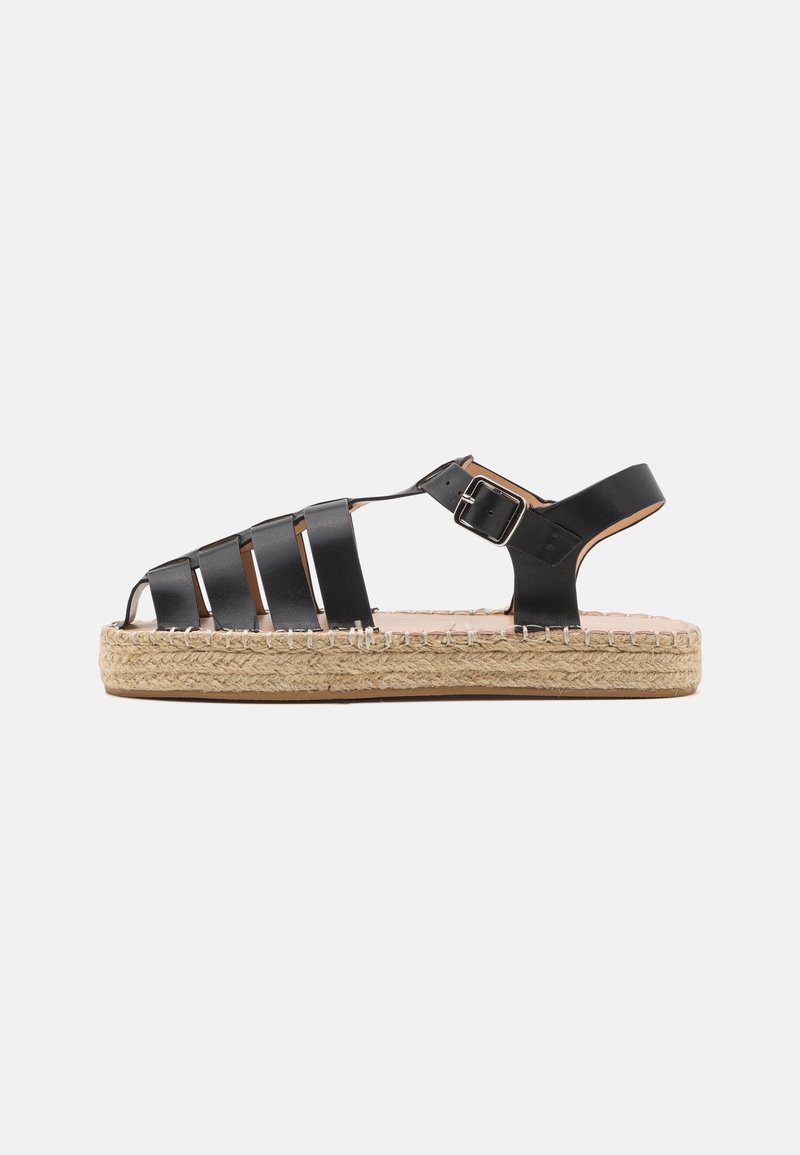 Sandale en cuir noir avec plusieurs brides, fermeture à boucle, et semelle plateforme en jute tressé, vue de côté sur fond blanc.