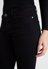 Jeans negre din denim cu o croială ajustată, având un închidere clasică cu buton, bucle pentru curea și detalii de cusătură subtile pe buzunare.