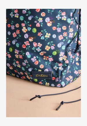 Tumesinine lillemustriga seljakott, kus on värvilised lillede ja kestade mustrid, siledat tekstuuri ja kuldne logo silt Cath Kidstonilt.