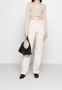 Un pull cropped beige avec des boutons, un jean blanc taille haute, et un sac à main en tissu noir. Des bottines noires à bout pointu complètent le look.