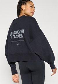 Sort cropped sweatshirt med overdimensionerede ærmer. Har hvid tekst på ryggen med teksten "WHATEVER IT TAKES." Blødt stof i bomuldsblanding.