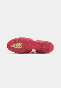 Bottines de football rouges avec des accents blancs, présentant une surface texturée et une semelle crantée. Quincaillerie dorée sur la plaque de crampons.