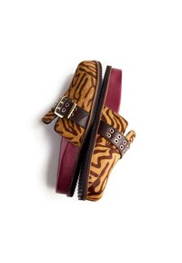 Des chaussures slip-on à motif zèbre brun et or, avec deux sangles brunes ajustables, des boucles métalliques et une semelle en caoutchouc bordeaux.