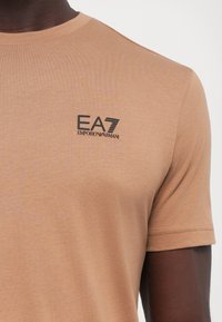 Kortermet t-skjorte i bomull, med svart EA7 Emporio Armani-logo på venstre bryst og klassisk rund hals.