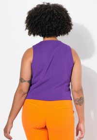 Top viola senza maniche con taglio dritto, abbinato a pantaloni arancioni aderenti con tasche posteriori. Texture liscia, senza motivi o accessori.