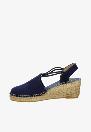 Navy blue suede wedge sandal with woven jute sole, slingback design, and crisscross straps. Features a rounded toe and textured surface.