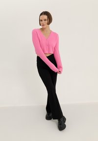 Rosa kort cardigan med knappar och långa ärmar, kombinerad med svarta flare-byxor och kraftiga svarta snörstövlar. Slät textur.