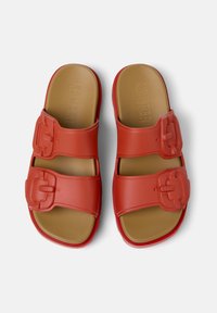 Red slide sandals with two wide straps featuring square-shaped buckles. Smooth rubber material with a brown cushioned insole.